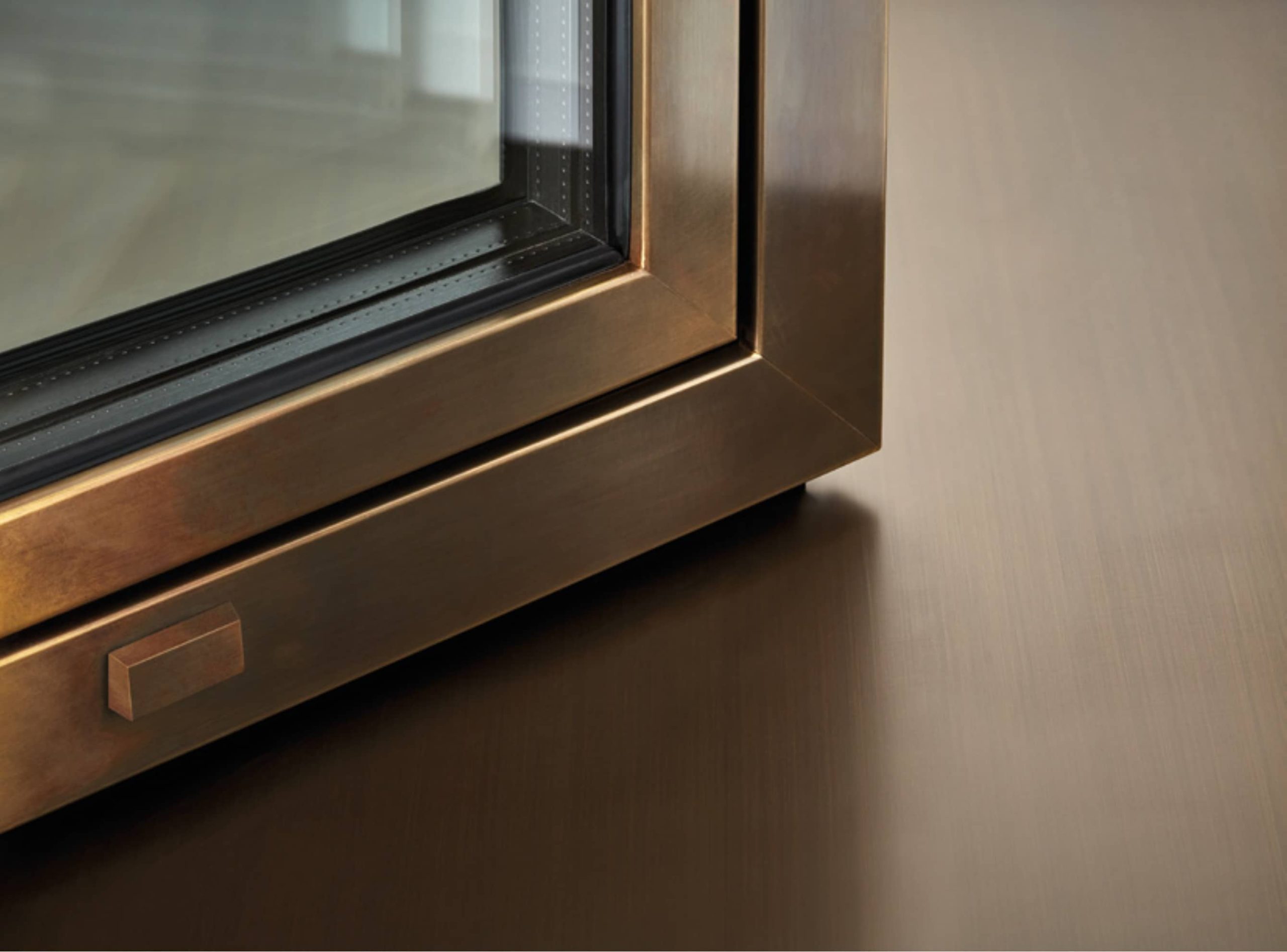 Close-up of a bronze-coloured aluminium window frame with a modern square-edged design and double-glazed unit, shown against a brushed metallic surface.